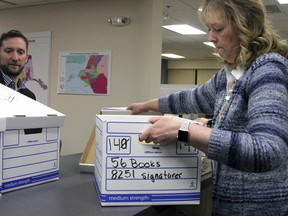 State Rep. Jason Green, left, looks on as Carol Thompson with the state Division of Elections in Anchorage, Alaska, unseals boxes containing more than 45,000 signature to get an initiative on the ballot this year to put financial and travel restrictions on Alaska lawmakers, Friday, Jan. 12, 2018. Elections workers will have to verify the signatures before the measure is approved for the ballot.
