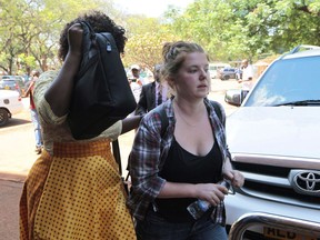FILE - In this Saturday, Nov. 4, 2017 file photo U.S. Citizen Martha O' Donovan, right, appears at the Harare Magistrates court escorted by a plain clothes police officer shielding her face in Harare. A Zimbabwean court on Thursday Jan. 4, 2018 freed "for now" an American woman charged with subversion for allegedly describing the former president on Twitter as a "sick man."