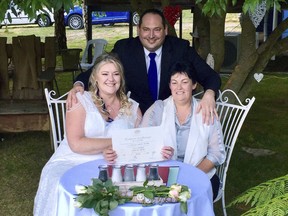 In this photo provided by Rodney Croome, Lainey Carmichael, left, Roz Kitschke, right, and celebrant Jason Betts pose as they show Lainey and Roz's marriage certificate at their home in Franklin, south of Hobart, Australia Tuesday, Jan. 9, 2018. Same-sex couples married in midnight ceremonies across Australia on Tuesday after the last legal impediment to gay marriage expired.