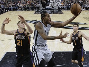 San Antonio Spurs forward Kawhi Leonard (2) scores as Phoenix Suns center Alex Len (21) and guard Devin Booker (1) defend during the first half of an NBA basketball game Friday, Jan. 5, 2018, in San Antonio. San Antonio won 103-89.