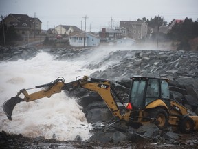 A backhoe tries to fill a hole in a retaining seawall in Cow Bay, NS after a night of heavy easterly wind hit the province.
