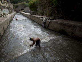 In this Nov. 30, 2017 photo, Douglas scoops up mud from the bottom of the polluted Guaire River, in search of gold and anything valuable he can sell, in Caracas, Venezuela. Some stretches of the river smell of sewer while others emit a toxic odor of fuel, a stench that stays in ones nose for hours after leaving the water.