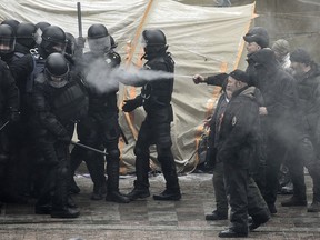 Protesters, right, use tear gas as they clash with police during a rally outside the Supreme Rada in Kiev, Ukraine, Tuesday, Jan. 16, 2018. At least one policeman has been injured and several protesters have been detained after scuffles outside the Ukrainian parliament to protest a new law governing the areas in the country's east under separatist control.