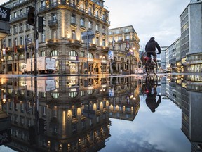 A man on a bicycle is mirrored in a puddle in downtown Frankfurt, Tuesday, Jan. 16, 2018.