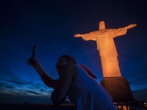 FILE - In this Nov. 25, 2017 file photo, a tourist takes a selfie with the Christ the Redeemer statue illuminated in orange to mark the International Day for the Elimination of Violence against Women, in Rio de Janeiro, Brazil. Starting Thursday, Jan. 25, Brazil is making it easier and cheaper for Americans to apply for a visa following a decline in the number of visitors from the U.S. in recent years.