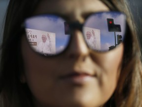 A banner welcoming Pope Francis is reflected in a woman's sunglasses as she waits for the pope's arrival at the Maquehue Air Base, in Temuco, Chile, Wednesday, Jan. 17, 2018. Francis heads to the heart of Chile's centuries-old conflict with indigenous peoples to celebrate Mass at the air base which is on contested land that was also used as a detention and torture facility during the country's bloody military dictatorship.