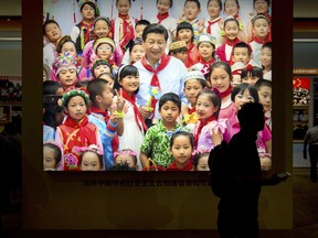In this Sept. 28, 2017, photo, a visitor walks past an illuminated photo showing Chinese President Xi Jinping surrounded by children at an exhibition highlighting five years of progress under Xi's leadership in Beijing. The birthrate in China fell in 2017 despite the country easing family limits and allowing all couples to have two children.