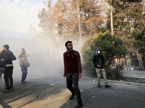 University students attend a protest inside Tehran University while a smoke grenade is thrown by anti-riot Iranian police, in Tehran on Saturday, Dec. 30, 2017.
