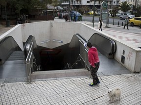 A woman with a dog looks on the shuttered entrance of a metro station during a strike by metro employees in Athens, on Monday, Jan. 15, 2018. Athenians are without public transport for the day and services nationwide face disruptions as Greek labor unions strike to protest further creditor-demanded measures due to be voted in Parliament.
