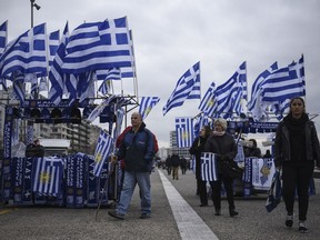 People walk between Greek flags ahead of a rally against the use of the term "Macedonia" for the northern neighbouring country's name, at the northern Greek city of Thessaloniki on Sunday, Jan. 21, 2018.  A flurry of recent talks between officials from the two countries, coupled with a new, more moderate government coming to power in Macedonia, have led to optimism that a solution might finally be within reach.