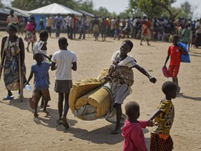 FILE - In this Friday, June 9, 2017 file photo, a South Sudanese refugee girl with a baby on her back carries a foam mattress to the communal tent where they will sleep, at the Imvepi reception center, where newly arrived refugees are processed before being allocated plots of land in nearby Bidi Bidi refugee settlement, in northern Uganda. International donors are threatening to withdraw funding for Uganda's South Sudanese refugee crisis over allegations that include misuse of relief items and the trafficking of girls and women, a government official said Tuesday, Feb. 6, 2018.