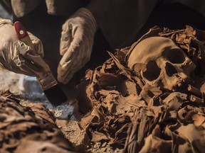 A picture taken on September 9, 2017 shows an Egyptian labourer unearthing mummies at a newly-uncovered ancient tomb for a goldsmith dedicated to the ancient Egyptian god Amun, in the Draa Abul Naga necropolis on the west bank of the ancient city of Luxor, which boasts ancient Egyptian temples and burial grounds.