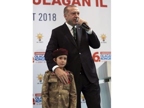 Turkish President Recep Tayyip Erdogan stands with a young girl in military uniform as he speaks to his ruling party members, in Kahramanmaras, Turkey, Saturday, Feb. 24, 2018.