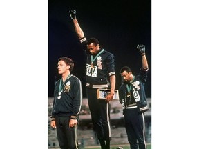 FILE - In this Oct. 16, 1968, file photo, extending gloved hands skyward in racial protest, U.S. athletes Tommie Smith, center, and John Carlos stare downward during the playing of national anthem after Smith received the gold and Carlos the bronze for the 200 meter run at the Summer Olympic Games in Mexico City. Australian silver medalist Peter Norman is at left.