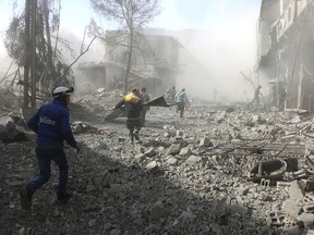 In this photo released on Tuesday Feb. 20, 2018 which provided by the Syrian Civil Defense group known as the White Helmets, shows members of the Syrian Civil Defense run to help survivors from a street that attacked by airstrikes and shelling of the Syrian government forces, in Ghouta, suburb of Damascus, Syria. (Syrian Civil Defense White Helmets via AP)