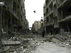 In this photo released on Thursday Feb. 22, 2018 which provided by the Syrian anti-government activist group Ghouta Media Center, which has been authenticated based on its contents and other AP reporting, shows Syrians walk between destroyed buildings during airstrikes and shelling by Syrian government forces, in Ghouta, a suburb of Damascus, Syria.