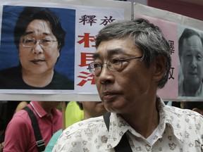 FILE - In this June 18, 2016, file photo, freed Hong Kong bookseller Lam Wing-kee stands next to a placard with picture of missing bookseller Gui Minhai, in front of his book store in Hong Kong as the protesters are marching to the Chinese central government's liaison office. Sweden has condemned China's "brutal" detention of a Swedish citizen who sold politically sensitive books and whose seizure while he traveled with diplomats stunned Western governments.