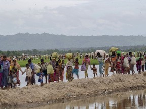 FILE -In this Oct. 19, 2017 file photo, Rohingya Muslims, who spent four days in the open after crossing over from Myanmar into Bangladesh, carry their belongings after they were allowed to proceed towards a refugee camp, at Palong Khali, Bangladesh. Six months after waves of attacks emptied Rohingya villages in Myanmar, sending 700,000 people fleeing into Bangladesh, there are few signs anyone is going home soon. Life isn't easy in the refugee camps, but the Rohingya living there have one immense consolation. "Nobody is coming to kill us, that's for sure," says one man.