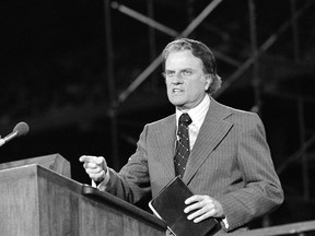 FILE - In this Oct. 24, 1976 file photo, Evangelist Billy Graham, 57, of Montreat, N.C., holds his bible while gesturing during the final service of the 10-day Southeastern Michigan Crusade at Pontiac Stadium, in Pontiac, Mich. Graham, who died Wednesday, Feb. 21, 2018, at his home in North Carolina's mountains at age 99, reached hundreds of millions of listeners around the world with his rallies and his pioneering use of television. Graham's body will be brought to his hometown of Charlotte on Saturday, Feb. 24, as part of a procession expected to draw crowds of well-wishers.