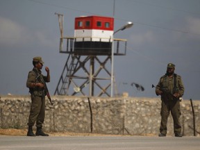 FILE - In this July 5, 2013 file photo, Palestinian Hamas security guards stand near an Egyptian watch tower on the border with Egypt in Rafah, southern Gaza Strip. The Egyptian army is bulldozing homes and olive groves in Feb. 2018 to build a buffer zone around the main airport in its troubled North Sinai Province, where Islamic State militants nearly killed the defense and interior ministers in December. The operation, described by residents and military officials, will displace thousands of residents from the hamlets around el-Arish airport, who are being moving to nearby cities where the army says they will receive compensation.