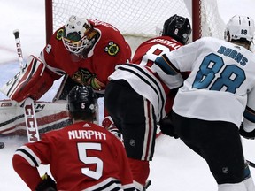 Chicago Blackhawks goalie J.F. Berube, left, blocks a shot by San Jose Sharks defenseman Brent Burns, right, during the first period of an NHL hockey game Friday, Feb. 23, 2018, in Chicago.