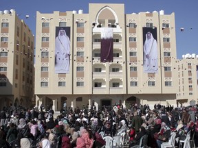 FILE - In this Jan. 16, 2016 photo, Palestinians gather at the Qatari-funded Hamad City housing complex in Khan Younis, southern Gaza Strip. Four years ago, Israel inflicted heavy damage on Gaza's infrastructure during a bruising 50-day war with Hamas militants. Now, fearing a humanitarian disaster on its doorstep, Israel is appealing to the world to fund a series of big-ticket development projects in the war-torn area. The banners show Qatar's Emir, Sheikh Tamim bin Hamad Al Thani, left, and his father, Sheikh Hamad bin Khalifa Al Thani.