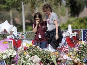 Margarita Lasalle, a bookkeeper and Joellen Berman, a guidance data specialist, look at a memorial Friday, Feb. 23, 2018 as teachers and school administrators returned to Marjory Stoneman Douglas High School for the first time since 17 victims were killed in a mass shooting at the school, in Parkland, Fla.
