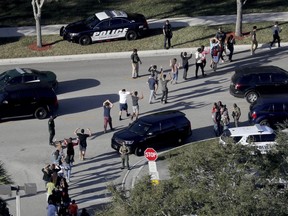 FILE - In this Feb. 14, 2018 file photo,  students hold their hands in the air as they are evacuated by police from Marjory Stoneman Douglas High School in Parkland, Fla., after a shooter opened fire on the campus.  Students are taught to evacuate during fire alarms but lock down during school shootings. So there was confusion Wednesday when a fire alarm sounded,  the second one that day at the high school as 19-year-old former student Nikolas Cruz unleashed a barrage of gunfire. Head for the exits or hunker down in classrooms?