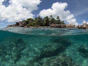 In this photo taken Tuesday, Feb. 20, 2018, a small island is seen above and below the water in the Seychelles. The tiny island nation of the Seychelles is announcing a pioneering marine conservation plan as part of a debt swap deal with creditors, designating nearly a third of its ocean waters as protected areas and aiming to ensure its unique biodiversity. (The Ocean Agency via AP)