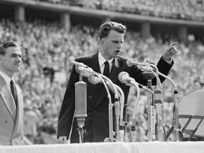 FILE - In this June 27, 1954 file photo, Evangelist Billy Graham speaks to over 100,000 Berliners at the Olympic Stadium in Berlin, Germany.   Graham, who transformed American religious life through his preaching and activism, becoming a counselor to presidents and the most widely heard Christian evangelist in history, has died. Spokesman Mark DeMoss says Graham, who long suffered from cancer, pneumonia and other ailments, died at his home in North Carolina on Wednesday, Feb. 21, 2018. He was 99.