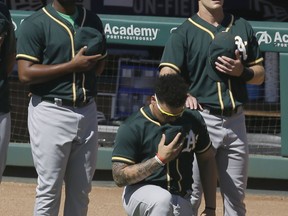 FILE - In this Sunday, Oct. 1, 2017 file photo, Oakland Athletics catcher Bruce Maxwell takes a knee during the national anthem next to teammates Mark Canha, right, and Raul Alcantara before a baseball game against the Texas Rangers in Arlington, Texas. Oakland Athletics catcher Bruce Maxwell says he will no longer kneel for the national anthem as he did last season as a rookie, when he became the first major leaguer to do so following the lead of many NFL players. He spoke Tuesday, Feb. 13, 2018 as the A's pitchers and catchers reported to spring training.