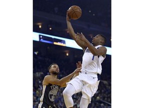 Dallas Mavericks' Dennis Smith Jr., right, lays up a shot over Golden State Warriors' Stephen Curry (30) during the first half of an NBA basketball game Thursday, Feb. 8, 2018, in Oakland, Calif.