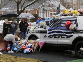 Mourners gather and leave flowers on a police cruiser parked in front of City Hall in Westerville, Ohio, on Sunday, Feb. 11, 2018. Westerville police officers Anthony Morelli and Eric Joering were killed in the line of duty Saturday when a suspect opened fire on them as they responded to a call at a residence.