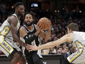 San Antonio Spurs' Patty Mills, center, from Australia, drives between Cleveland Cavaliers' Jeff Green, left, and Kyle Korver in the first half of an NBA basketball game, Sunday, Feb. 25, 2018, in Cleveland.
