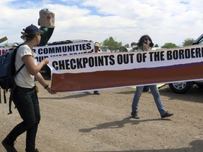 FILE - In this May 27, 2015, file photo, two protesters carry a large banner as they walk toward a U.S. Border Patrol checkpoint on a two-lane road in Amado, Ariz., about 20 miles north of the Mexican border. The U.S. Circuit of Appeals for the Ninth Circuit says it lacked the information necessary to decide if a U.S. Border Patrol enforcement zone around a highway checkpoint in southern Arizona was a nonpublic forum as argued by the District Court in Arizona in a case that arose from roadside protests.