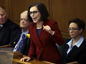 FILE - In this Jan. 9, 2017, file photo, Oregon Gov. Kate Brown delivers her inaugural speech in the Capitol House chambers in Salem, Ore. People convicted of stalking and domestic violence or with restraining orders in Oregon will not be able to buy or own guns or ammunition after the Senate passed a bill which next goes to Gov. Kate Brown for her signature. At right is House Speaker Tina Kotek and on left is Senate President Peter Courtney, both Democrats.