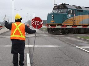 A man holds a stop sign near the rail crossing at the Woodroffe Barrhaven crossing in Ottawa on May 11, 2015.