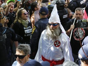 This July 8, 2017 photo shows members of the KKK escorted by police past a large group of protesters during a KKK rally in Charlottesville, Va.