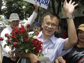 FILE - In this May 11, 2011 file photo, historian Somsak Jeamteerasakul holds flowers from his supporters as he walks out of a police station, where police heard about an article he wrote about a Thai royal family member, in Bangkok, Thailand. A Thai legal aid group said Monday, Feb. 19, 2018,  that a caricature of historian Somsak Jeamteerasakul, a critic in exile of Thailand's monarchy, was auctioned online  for $6,400 to be used to bail out political prisoners.