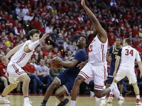 Michigan's Zavier Simpson, center, drives past Wisconsin's Ethan Happ, left, and Khalil Iverson during the first half of an NCAA college basketball game Sunday, Feb. 11, 2018, in Madison, Wis.
