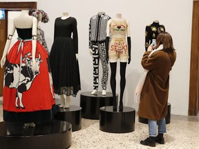 A woman takes pictures to designer clothes displayed at the exhibit "Italiana, Italy seen from fashion", an exposition that aims to show the evolution of Italy, its culture and its people through fashion from 1971 to 2001, unveiled in Milan, Italy, Thursday, Feb. 22, 2018.