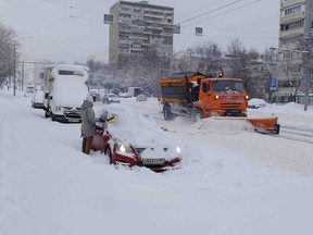 A woman clears snow from her car during heavy snowfall in Moscow, Russia, Sunday, Feb. 4, 2018. Heavy snow and freezing rain have knocked down thousands of trees in the Russian capital and one person is reported to have been killed.