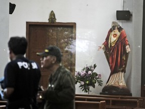 In this image shot through a glass window, police investigators examine the interior of St. Lidwina Church that was damaged following an attack in Sleman, Yogyakarta province, Indonesia, Sunday, Feb. 11, 2018. Police shot a sword-wielding man who attack the church during a mass, injuring a number of people including a German priest. The reason for the attack Sunday morning was not immediately clear. (AP Photo)