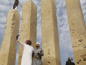 In this Saturday, Feb. 3, 2018 photo, officials take a selfie as a Yemeni militiaman stands atop a limestone column at the Awwam Temple, also known as the Mahram Bilqis, in Marib, Yemen. Experts fear the temple, as well as other historic and cultural wonders across Yemen beyond those acknowledged by international authorities, remain at risk as the country's stalemated Saudi-led war against Shiite rebels rages on.