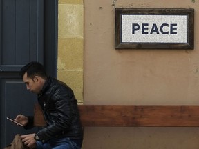 A man uses his mobile phone as sits on a bench next to a "Peace" sign in central capital Nicosia, Cyprus, Friday, Feb. 2, 2018. Barely seven months on from the latest failure to reunify the east Mediterranean island nation of Cyprus, Greek Cypriots are gearing up for a presidential election, skeptical about whether anyone can lead them out of the labyrinth of the decades-old division.