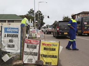 A woman crosses the road near newspaper headlines in Harare, Zimbabwe Thursday, Feb, 15, 2018. Zimbabwean opposition leader Morgan Tsvangirai died Wednesday at age 65, ending a long campaign to lead his country that brought him jailings, beatings and accusations of treason.
