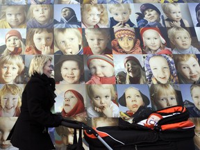 A mother pushing a stroller by a wall with portraits of children in Reykjavik.