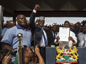 FILE - In this Tuesday, Jan. 30, 2018 file photo, opposition politician Miguna Miguna, center, raises his fist as a gesture to the crowd as he stands next to opposition leader Raila Odinga, center right, and politician James Orengo, far right, as Odinga holds an oath during a mock "swearing-in" ceremony at Uhuru Park in downtown Nairobi, Kenya. Miguna said Wednesday, March 28, 2018 that he is detained in a toilet at the country's main airport after he refused an attempt to deport him.