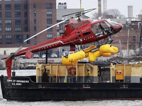 A helicopter is hoisted by crane from the East River onto a barge, Monday, March 12, 2018, in New York.