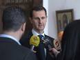 This photo provided by the official Facebook page of the Syrian Presidency, Syrian President Bashar Assad, centre, speaks with reporters, in Damascus, Syria, Sunday, March 4, 2018.